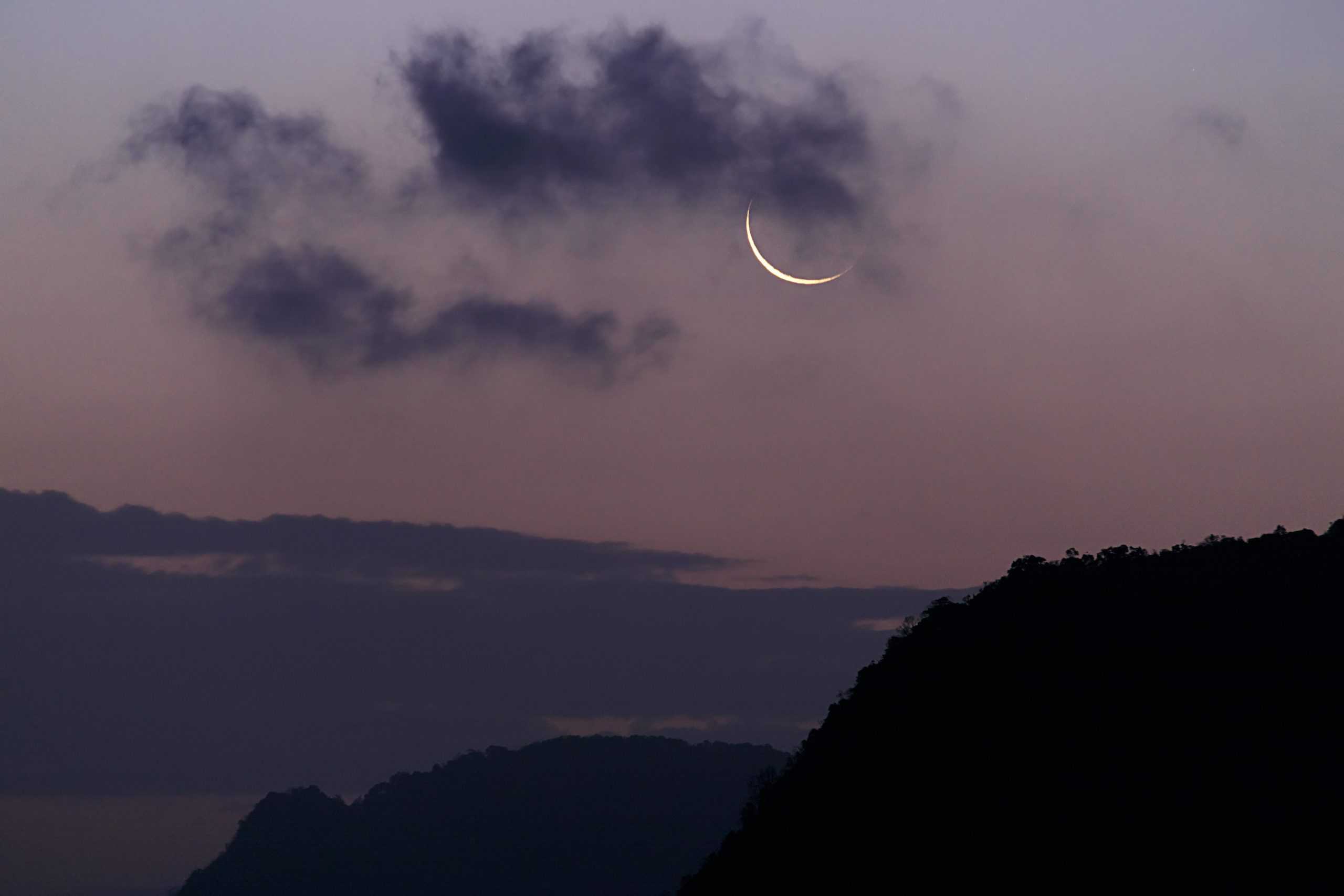 A crescent moon rises over silhouetted mountain peaks at dusk, evoking stillness and contemplative peace.